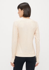 Heled beige pikkade varrukate spordipluus, millel on peene tekstuurne muster, ümmargune kaelus ja pöidlaholesid alt. Sile ja veniv materjal.