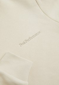 Felpa beige con polsini a coste, caratterizzata da un logo ricamato "Peak Performance" in una tonalità coordinata. Texture liscia, design semplice.