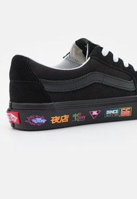 Černé tenisky Vans s bílými tkaničkami, černým pruhem a barevn�ými neonovými grafikami na podrážce, včetně nápisů "Off The Wall" a "Since 66".