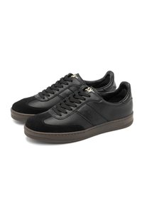 Un paio di sneakers in pelle nera a bassa punta con pannelli laterali testurizzati, punte in suede, lacci neri e suole in gomma marrone.