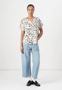 Lett, kremfarget bluse med svart blomstermønster, korte ermer, V-hals, parret med løse, lyseblå jeans og svarte lofas.