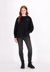 Černá oversized mikina s kulatým výstřihem a dlouhými rukávy, doplněná černými úzkými džíny a černými šněrovacími botami. Minimalistický design.