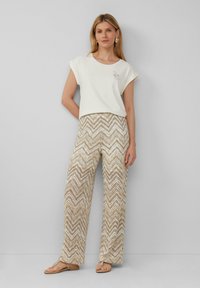 Haut créme à manches courtes avec une broderie en forme d'abeille, associé à un pantalon large à motif zigzag marron clair. Sandales à fines lanières.
