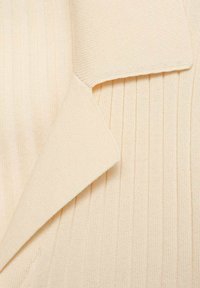 Primo piano di un tessuto rigato crema con un dettaglio del colletto piegato, che mette in risalto una consistenza liscia e linee verticali su tutto il materiale.