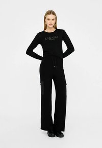 Mustast tekstuurse logoga pika varrukaga särk ja mustad laiade jalgadega püksid küljetaskutega, mõlemad pehmest kangast. Mustad jalatsid täiendavad komplekti.