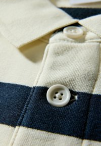 Koszula z krótkim rękawem w kremowo-granatowy paskowany wzór, z plisą na guziki z białym, czteroodkrowym guzikiem oraz kołnierzykiem.