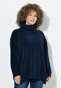 Maglione a collo alto blu navy con una finitura morbida e testurizzata, vestibilità ampia e spacchi laterali, abbinato a jeans in denim.