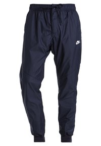 Námorní modré Nike joggingové kalhoty vyrobené z lehkého, hladkého materiálu. Mají elastický pas se šňůrkou a bílé logo na stehně.