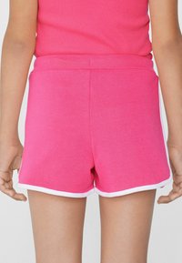 Des shorts en coton rose présentent une bordure blanche, une texture douce et une coupe décontractée. La taille est élastique, garantissant confort et aisance.