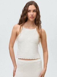 Top court blanc avec un col en forme de vagues, arborant un motif tricoté texturé. Associé à une jupe à pois assortie.