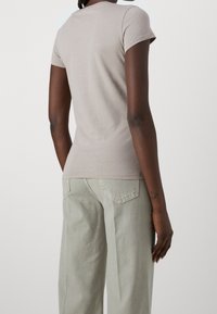 Camiseta de manga corta en tono topo claro, hecha de una tela suave, con cuello redondo, corte ajustado y costuras mínimas para una silueta suave.
