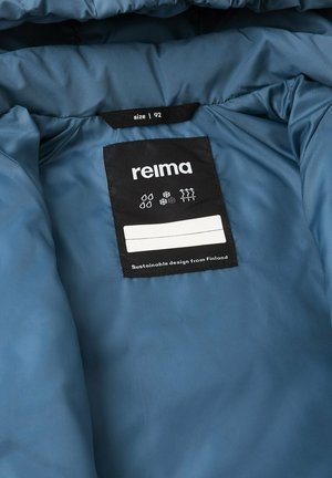 Interno di una giacca imbottita blu che presenta un'etichetta nera con testo bianco e simboli di cura. Il materiale appare liscio con una finitura opaca.