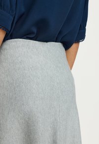 Blusa blu navy con maniche corte arricciate, abbinata a una gonna a vita alta grigio chiaro, testurizzata con una finitura liscia.