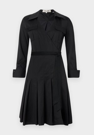 Vestido preto envolvente com mangas longas, colarinho, dois bolsos no peito e um cinto na cintura. Apresenta uma saia plissada para dar mais textura e movimento.