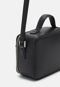 Borsa in pelle nera con forma rettangolare, dettagli testurizzati e una zip argentata su un lato. Dotata di un manico corto e di una tracolla.