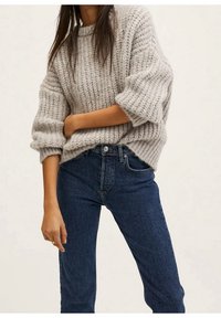 Pull en tricot épais gris avec une coupe décontractée, manches retroussées, associé à un jean en denim foncé. Tissu texturé et silhouette ample.
