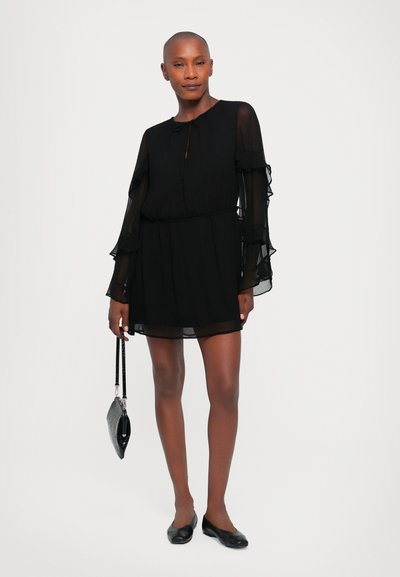 Black chiffon dress with long ruffled sleeves, elastic waist, and a round neckline. Paired with black flats and a textured handbag.