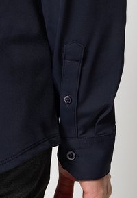 Marineblauw shirt met lange mouwen van een gestructureerde stof, met knoopsluitingen aan de manchetten en een patchdetail op de mouw met een strak ontwerp.