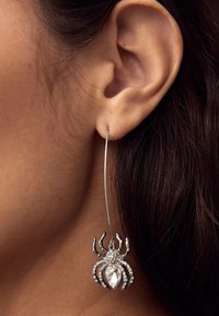 Spider-shaped earring in silver tone with clear rhinestones, featuring a curved wire design and hanging pendant accent.
