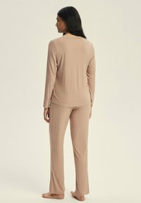 Beige ribbed loungewear set with long sleeves and pants, featuring soft texture and relaxed fit, viewed from the back.