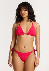 Roze bikini set met een structuur in golfpatroon. Triangle top met dunne bandjes, gecombineerd met low-rise broekjes met strikdetails aan de zijkanten.