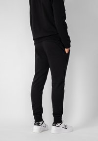 Pantalones jogger negros hechos de un tejido suave, con un diseño ajustado, bolsillos laterales y puños acanalados. Combinados con zapatillas blancas.