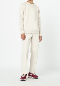 Helles beiges Sweatshirt, kombiniert mit passenden Hosen und burgunderfarbenen Sneakers. Das Sweatshirt hat ein kleines Logo auf der Brust.