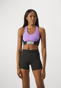 Lilla treningstop med svarte detaljer, som har en logobånd. Kombinert med høyt liv svarte shorts, glatt stoff, tettsittende design.