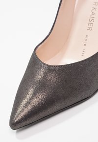 Escarpin noir à bout pointu en tissu métallique texturé, présentant un design élégant avec une légère brillance et une doublure intérieure lisse.