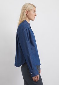 Denimhemd in Dunkelblau, mit klassischem Kragen, durchgehender Knopfleiste und langen Ärmeln mit geknöpften Manschetten. Gerader Schnitt mit lockerer Passform.