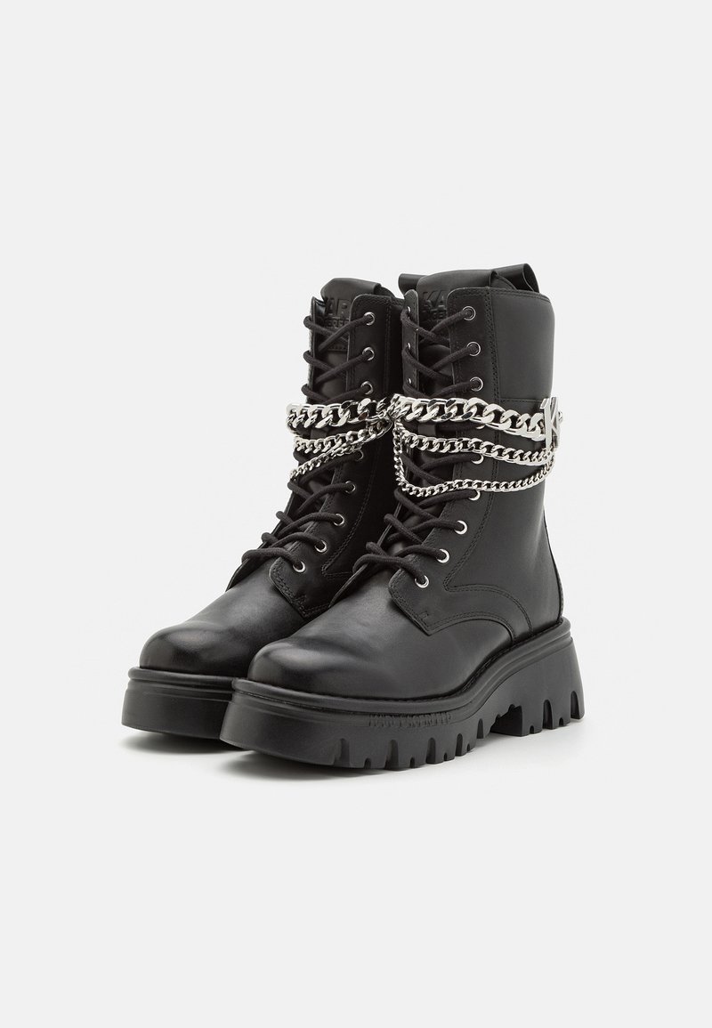 Schwarze Lederkampfstiefel mit einer robusten Sohle, die silberne Kettenverzierungen um den Knöchel und ein klassisches Schnürdesign aufweisen.