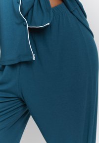 Teal, ribbed lounge set featuring a relaxed fit. The top has button details and elastic waistband; drawstring accent on pants.