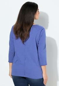Blauw langslijfshirt met een eenvoudig ontwerp, zachte textuur en een naaddetail op de rug. Draag het met een donkere spijkerbroek in een neutrale omgeving.