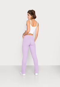 Calças flared em lilás claro, com uma cintura elástica, combinadas com um top cropped branco, vistas de costas contra um fundo neutro.