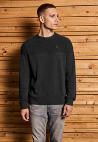 Dunkelgrauer gestrickter Pullover mit geripptem Muster, Rundhalsausschnitt und horizontalem Streifenmuster über der Brust. Mit kleinem Logo.