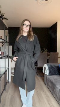 Crni, dugi, kaput opuštenog kroja s remenom, sa bočnim džepovima i reverima, nosi se preko crne košulje i svijetloplavih hlača.