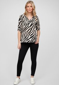 Black and beige zebra-patterned top with a V-neck and silver zipper detail, paired with black leggings and white sneakers.
