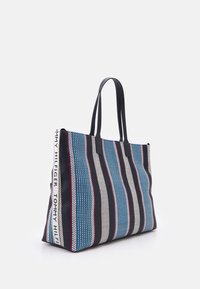 Randig strandväska med blå, röd och vita mönster. Tillverkad av vävd tyg med hållbara svarta handtag och Tommy Hilfiger-logotyp.