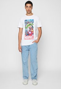 Hvid bomulds t-shirt med et farverigt Marvel-graphic på fronten, sammen med lyseblå denim jeans og hvide sneakers.