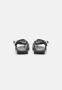 Sandali neri in pelle con cinturini intrecciati, suola piatta, fibbia regolabile alla caviglia e design minimalista senza decorazioni.