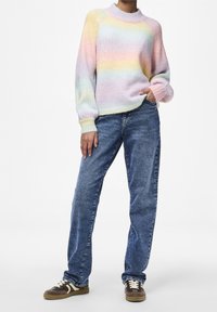 Pull tricoté rayé aux tons pastel avec un col montant, manches longues et poignets côtelés, associé à un jean bleu délavé et des baskets marron.