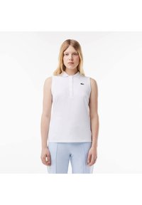 Polo shirt bianco senza maniche con colletto e chiusura a bottoni, caratterizzato da un logo verde ricamato sul lato sinistro del petto. Tessuto con texture liscia.