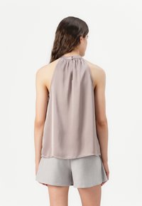 Hellgraues ärmelloses Oberteil mit drapierter Rückseite, weichem Material und gerafftem Ausschnitt. Kombiniert mit hellgrauen Shorts, beide im minimalistischen Design.