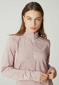 Helles rosa Langarmshirt mit einem Reißverschlusskragen, strukturiertem Stoff mit einem subtilen Muster und Daumenlöchern in den Ärmeln.