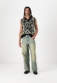 Mouwloze sweater in een zwart-wit dierenprint, gecombineerd met lichtblauwe, losvallende denim jeans. Zwarte schoenen maken de outfit compleet.