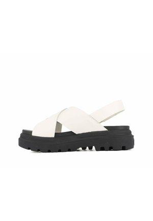 Sandales blanches à brides croisées avec une surface texturée et une semelle en caoutchouc noire présentant un design épais et un profilant à motifs.