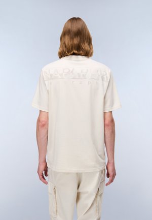 Beige T-shirt with short sleeves and a crew neckline, featuring a subtle logo print in lighter shade on the back. Soft fabric.