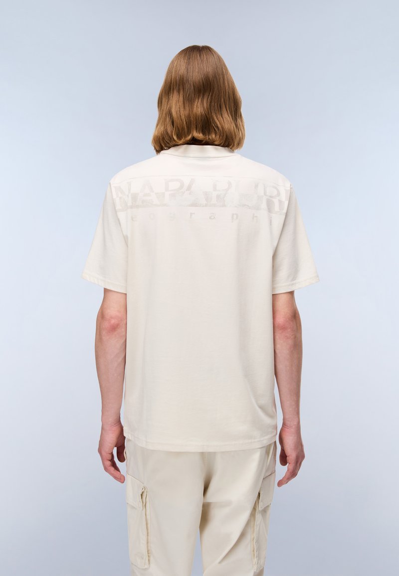 Beige T-shirt with short sleeves and a crew neckline, featuring a subtle logo print in lighter shade on the back. Soft fabric.