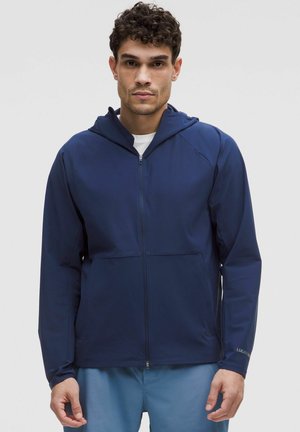 Marineblaue Zip-Hoodie-Jacke mit glatter Textur, ausgestattet mit Raglanärmeln und zwei Fronttaschen, entworfen für Aktivitäten im Freien.