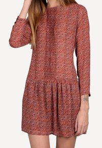 Långärmad klänning i knälängd av strukturerad röd och lila tyg, med en rynkad midja och vertikala veck på bysten.